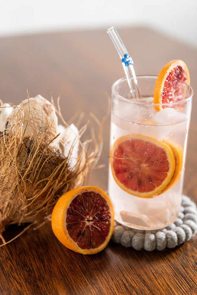 glass with straw containing blood orange next to coconut